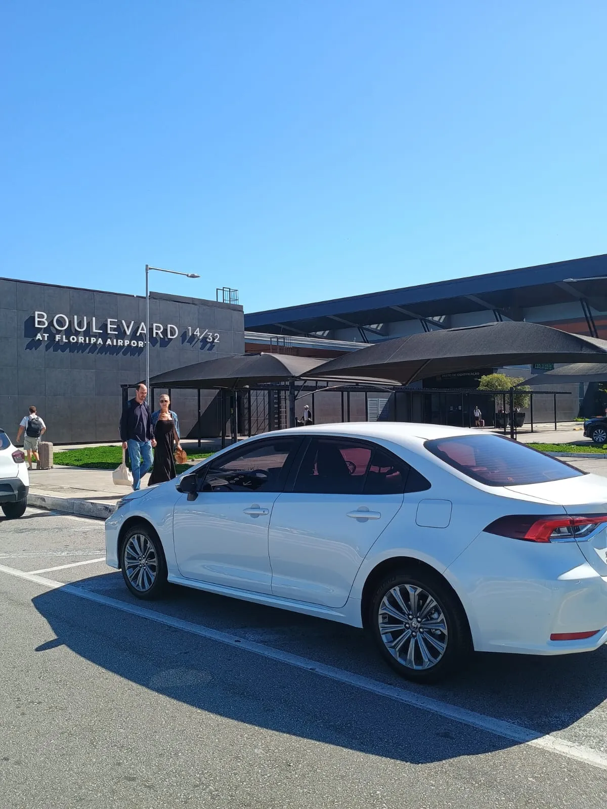 Toyota Corolla branco estacionado em frente ao Boulevard 14/32, no Aeroporto de Florianópolis