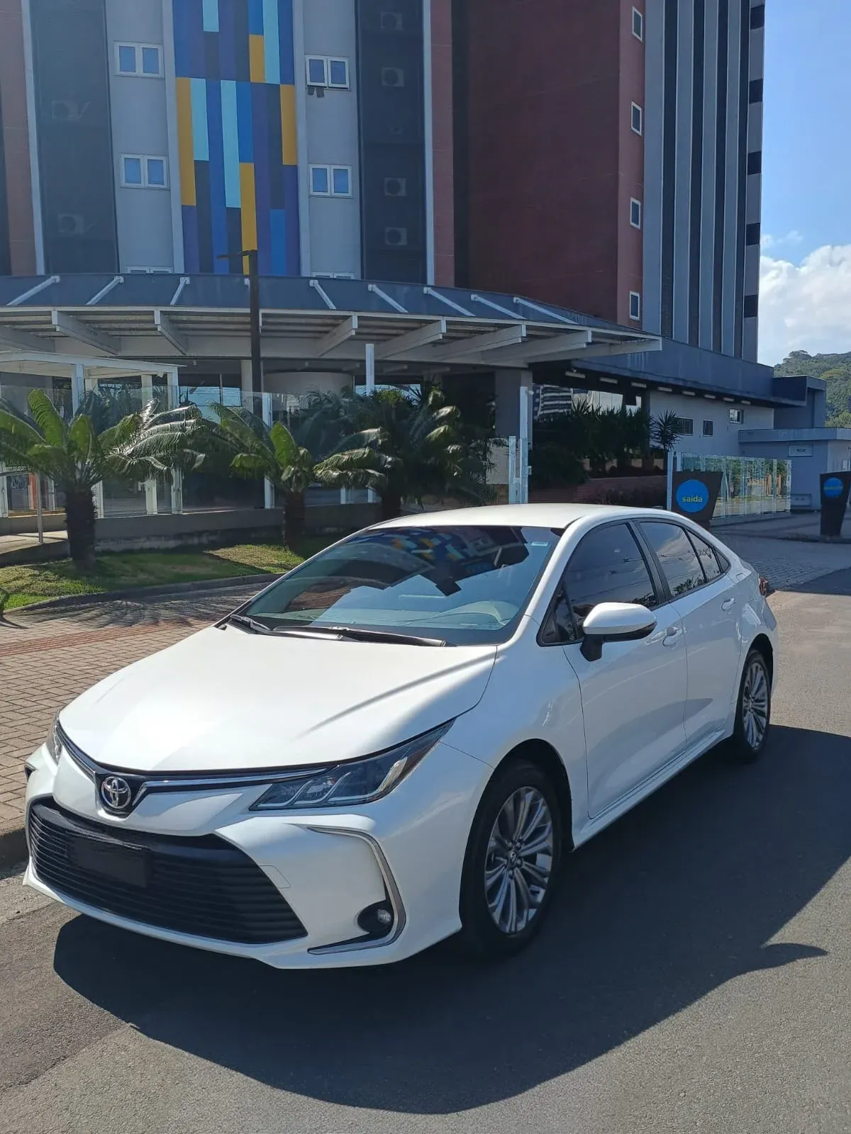 Toyota Corolla branco de frente, estacionado diante de um hotel