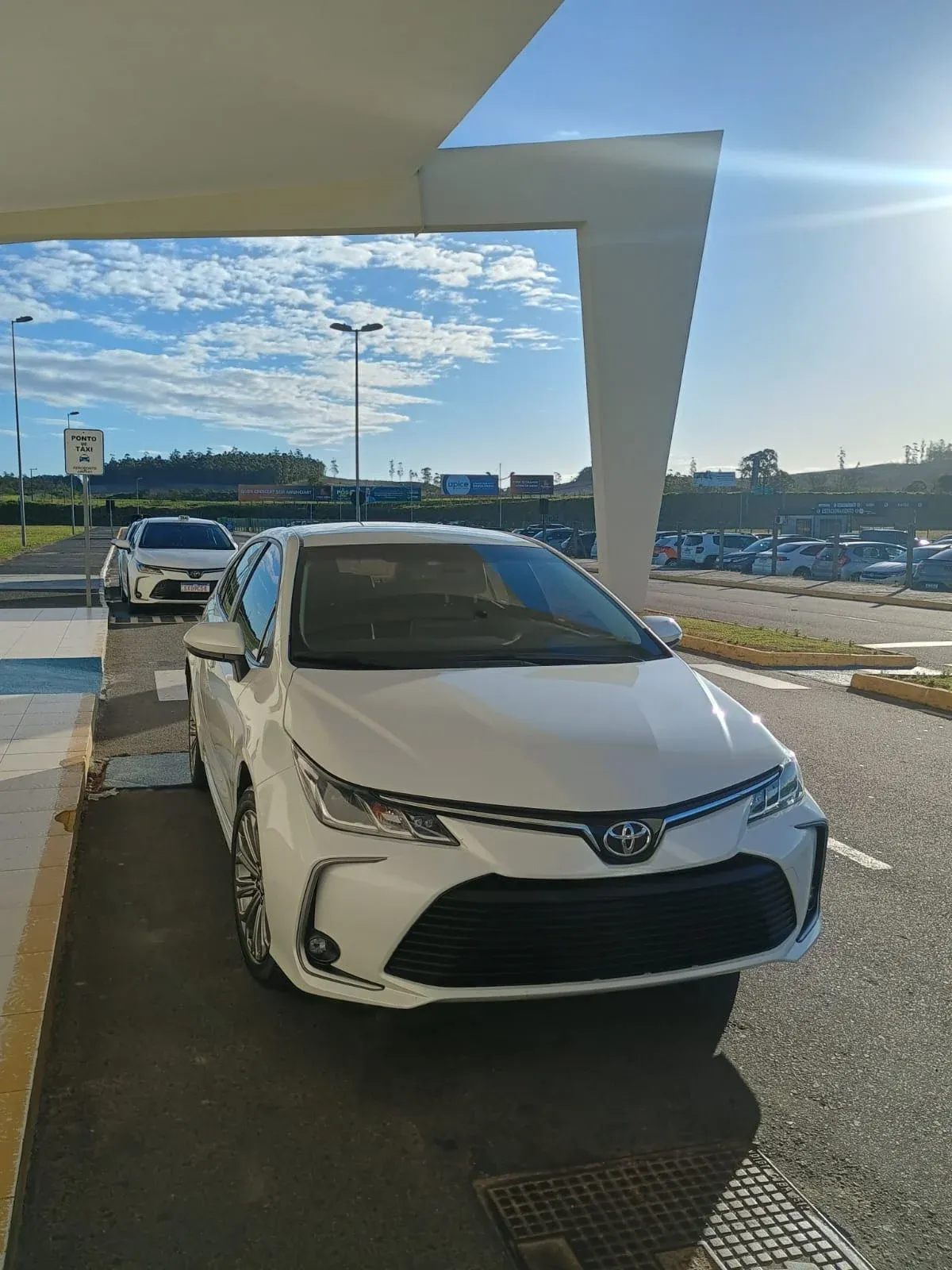 Toyota Corolla branco parado sob a marquise de embarque de um aeroporto
