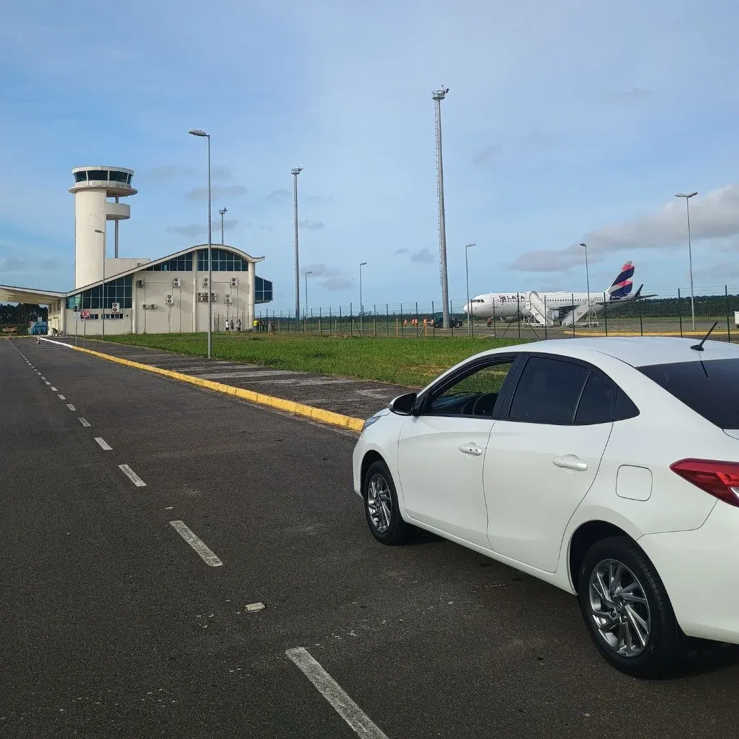 Toyota Corolla branco na pista de acesso de um aeroporto regional, com a torre de controle ao fundo